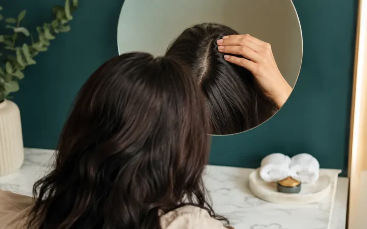 امرأة تفحص فرق الشعر في المرآة لمعرفة أسباب تساقط الشعر عند النساء